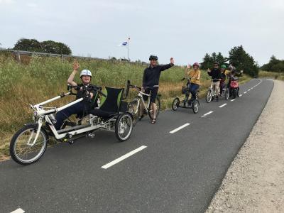 Fem voksne på tur på handicap-cykler. De vinker til kamera.